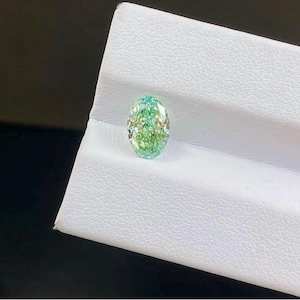 Può includere: Una gemma sciolta a taglio ovale caratterizzata da una vibrante tonalità verde menta con sfaccettature interne che creano una superficie scintillante e riflettente. La pietra mostra una brillante chiarezza e un profilo di colore verde chiaro.