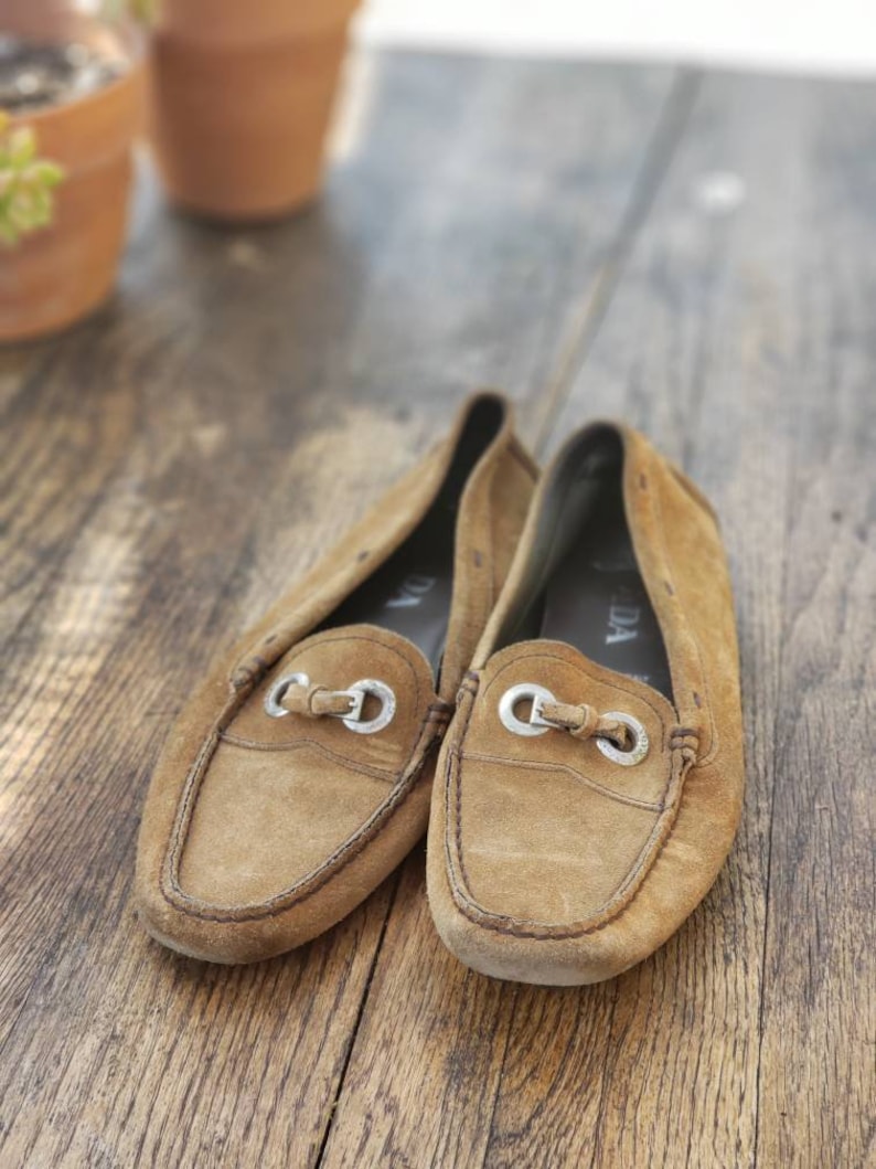 May include: A pair of brown suede loafers with silver buckles. The loafers are worn and have a distressed look.