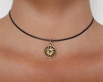May include: A gold sun pendant necklace on a black leather cord.