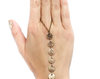 May include: A gold chain bracelet with a series of round metal charms hanging from it. The bracelet is worn on a hand with gold glitter nail polish.