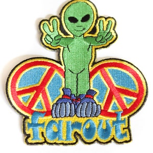 Könnte beinhalten: Gestickter Aufnäher mit einer grünen Alienfigur, die das Friedenszeichen zeigt. Der Alien befindet sich über zwei Friedenssymbolen mit roten und blauen Details. Das Wort "Far Out" ist in Blau und Gelb gestickt.