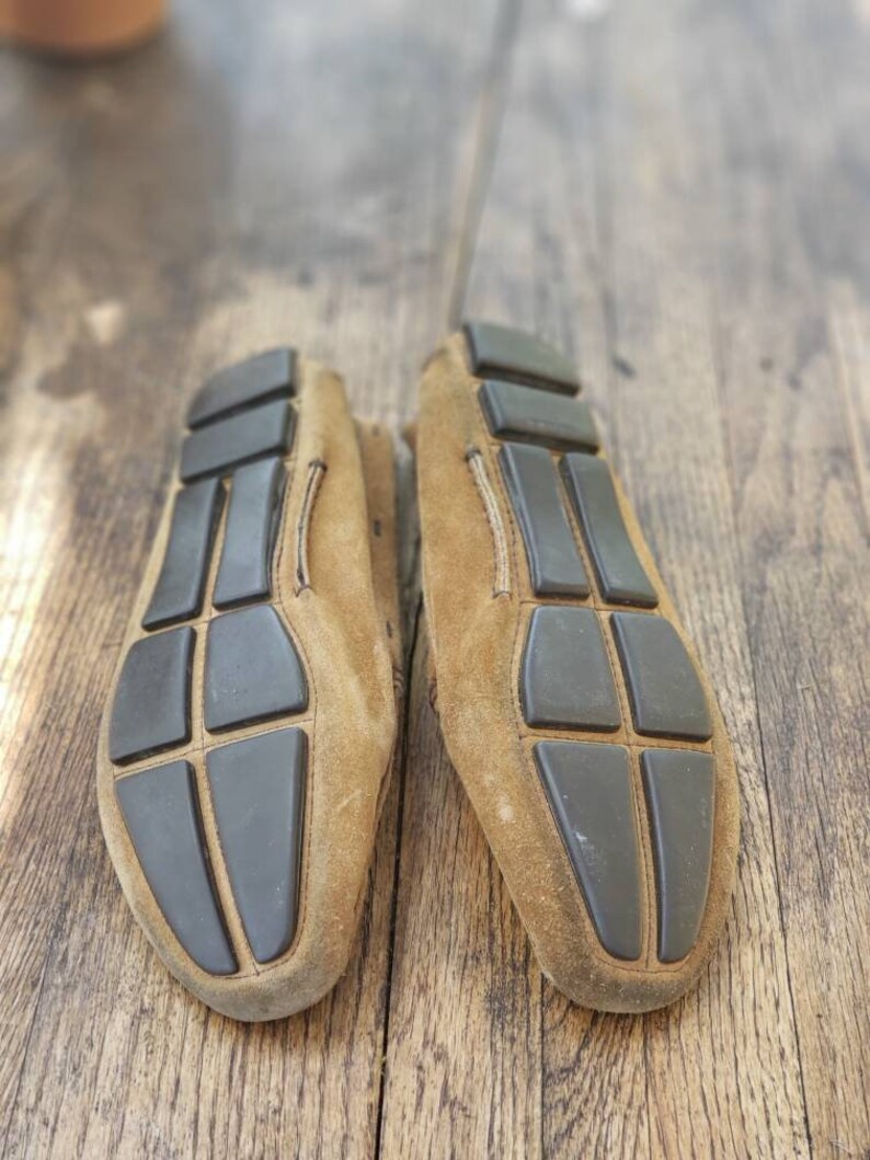 May include: A pair of brown suede loafers with black rubber soles. The soles have a grid pattern.