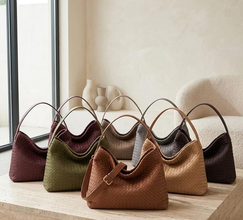 May include: A collection of seven hobo-style handbags featuring a woven texture pattern. The bags are displayed in various colours including burgundy, olive green, tan, beige, grey, and dark brown, each with a single shoulder strap and buckle.