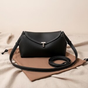 Black pebbled leather shoulder bag on cloth, adjustable strap coiled beside, minimalist crossbody purse