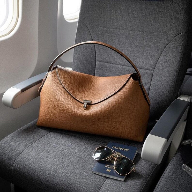 Tan pebbled leather shoulder bag draped on office chair, top handle leather bag with sunglasses and strap