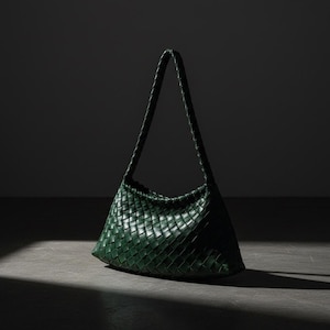 May include: A dark green shoulder bag featuring an intricate woven leather construction. The bag has a structured, curved base and a single, integrated braided strap that extends from the top sides, creating a cohesive, uniform appearance.
