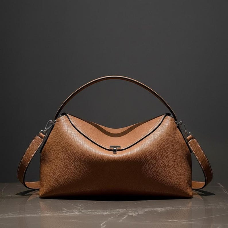 Studio lit warm tan pebbled leather shoulder bag, structured crescent shoulder bag with curved top handle