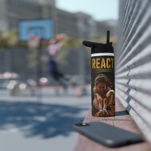 May include: A black water bottle with a black lid and straw, featuring the gold text "REACT" above a graphic of a person playing volleyball. The bottle has a cylindrical shape and is positioned upright on a wooden surface next to a smartphone.