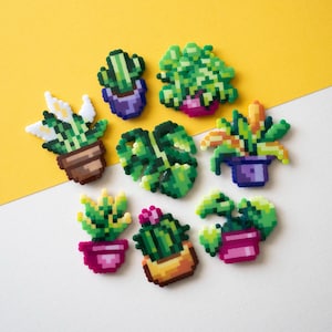 May include: A collection of eight pixel art style plant ornaments in various pots. The designs feature green foliage, cacti, and succulents in shades of lime, forest green, and yellow, set in purple, pink, brown, and orange containers.