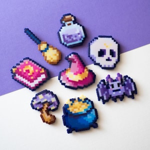 Puede incluir: Un conjunto de ocho dijes estilo pixel art que incluyen una botella de poción, una escoba, un libro de hechizos, un sombrero de bruja, una calavera, un murciélago, un hongo y un caldero lleno de monedas de oro, con colores vivos y bordes cuadrados.