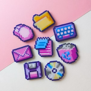 Pode incluir: Um conjunto de oito pins de arte em pixel com ícones de computador, incluindo uma pasta amarela, um rato rosa, um teclado roxo, um envelope rosa, um documento azul, um cesto rosa, uma disquete roxa e um disco compacto multicolorido com bordas escuras.