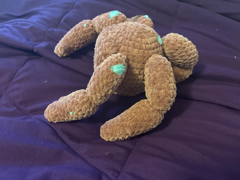 May include: A brown plush toy with a soft, textured surface and multiple limbs. The stuffed creature features small, light teal accents on the tips of its appendages and joints, providing a subtle contrast to the solid brown color of the body.