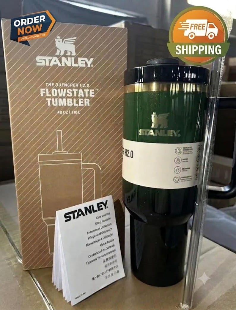 May include: A dark green Stanley The Quencher H2.0 FlowState tumbler with a black lid and handle, accompanied by its cardboard packaging box, a clear plastic straw, and a white care and use instruction booklet with the Stanley brand logo.