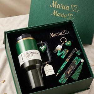 May include: A dark green gift box containing a Stanley Quencher H2.0 tumbler, a letter M keychain, a pen, and a bookmark. The items feature green and black marbled resin with gold accents. The name Maria is printed on the box and items.