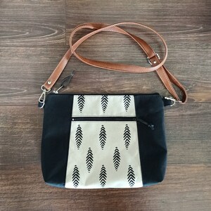 May include: A black and white patterned crossbody bag with a brown leather strap. The bag has a zipper closure and a small pocket on the front.