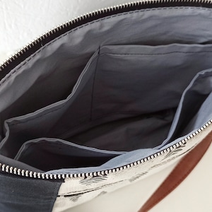 May include: A black and white patterned bag with a brown leather strap. The bag has a zipper closure and a gray fabric lining with multiple pockets.