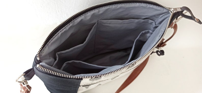 May include: A black and white patterned bag with a brown leather strap. The bag has a zipper closure and a gray fabric lining with multiple pockets.