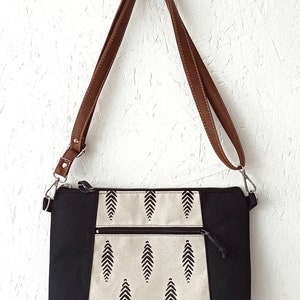 May include: A black and white patterned crossbody bag with a brown leather strap. The bag has a zipper closure and two pockets on the front.