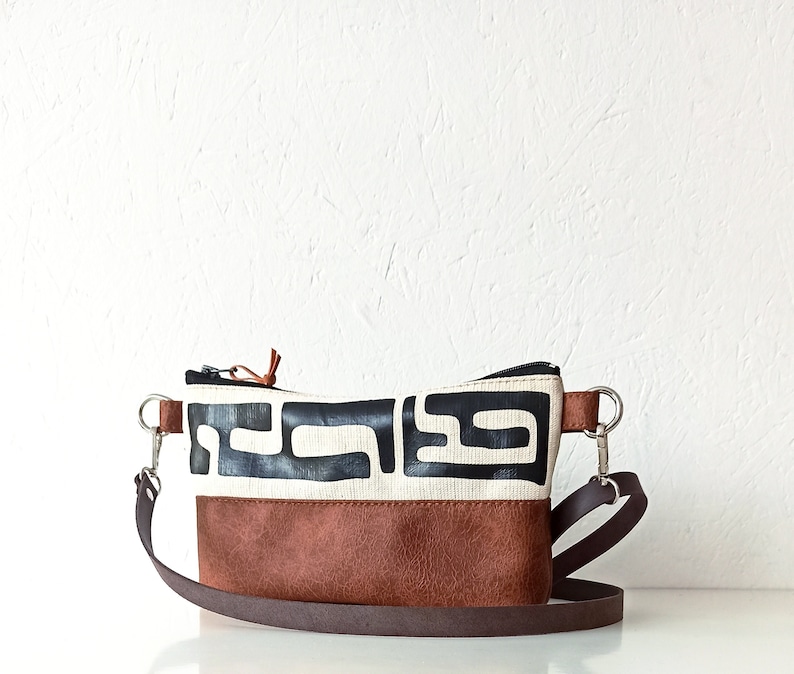 Pode incluir: Uma pequena bolsa transversal retangular com fundo de couro marrom e se&ccedil;&atilde;o superior branca com um padr&atilde;o geom&eacute;trico preto. A bolsa tem uma al&ccedil;a marrom e ferragens prateadas. A bolsa tem aproximadamente 23 cm de largura.