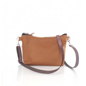 May include: A brown canvas crossbody bag with a zipper closure and a brown adjustable strap.