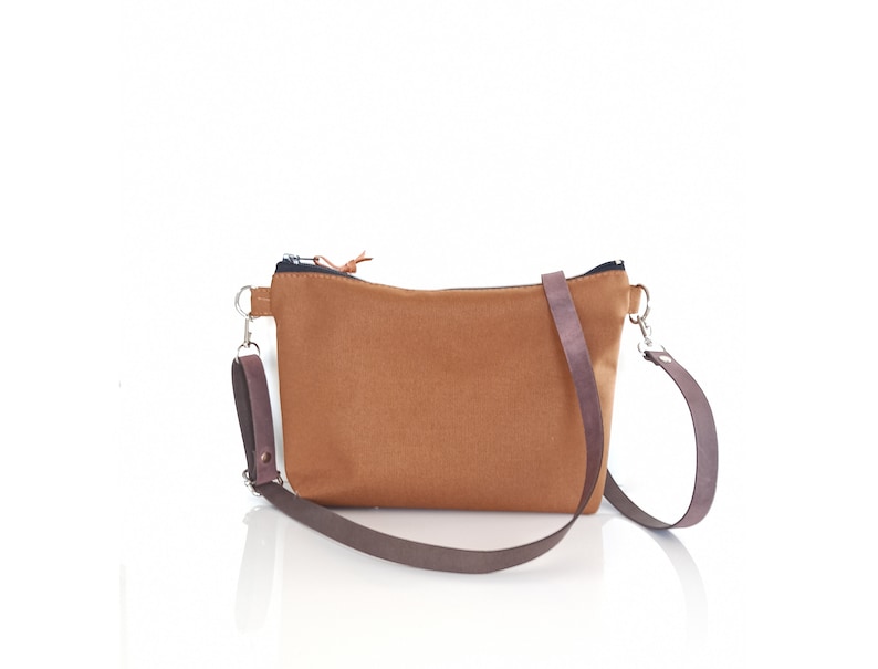 May include: A brown canvas crossbody bag with a zipper closure and a brown adjustable strap.