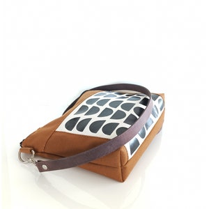 May include: A brown and white canvas tote bag with a black geometric pattern. The bag has a brown leather strap.