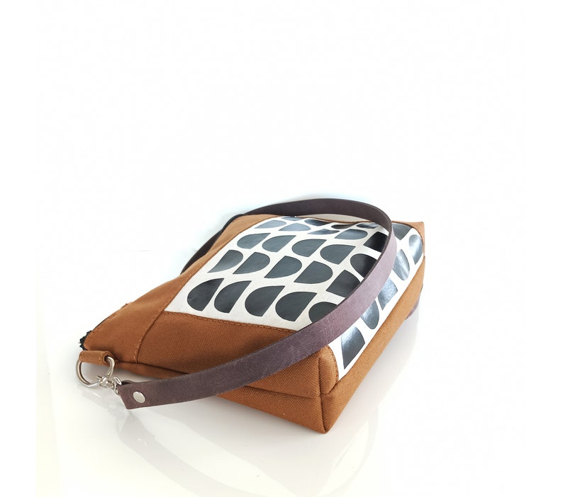 May include: A brown and white canvas tote bag with a black geometric pattern. The bag has a brown leather strap.