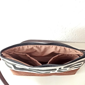 Pode incluir: Vista aberta de uma bolsa transversal com padr&atilde;o marrom e branco com z&iacute;per preto. A bolsa tem uma base de couro marrom e uma al&ccedil;a marrom. O interior possui v&aacute;rios bolsos e um forro marrom claro.