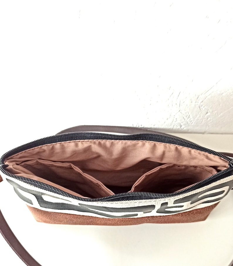 Pode incluir: Vista aberta de uma bolsa transversal com padr&atilde;o marrom e branco com z&iacute;per preto. A bolsa tem uma base de couro marrom e uma al&ccedil;a marrom. O interior possui v&aacute;rios bolsos e um forro marrom claro.