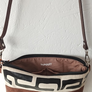 Pode incluir: Bolsa transversal aberta com um padr&atilde;o geom&eacute;trico em preto e branco. A bolsa tem uma base e uma al&ccedil;a de couro marrom. O interior &eacute; marrom com o texto "byMART".