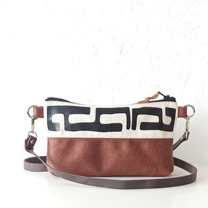 Pode incluir: Bolsa transversal retangular com base em couro marrom e se&ccedil;&atilde;o superior creme com um padr&atilde;o geom&eacute;trico preto. A bolsa tem uma al&ccedil;a ajust&aacute;vel marrom e ferragens prateadas.