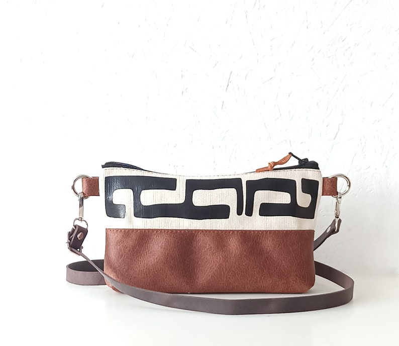Pode incluir: Bolsa transversal retangular com base em couro marrom e se&ccedil;&atilde;o superior creme com um padr&atilde;o geom&eacute;trico preto. A bolsa tem uma al&ccedil;a ajust&aacute;vel marrom e ferragens prateadas.