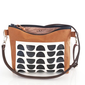 May include: A brown canvas crossbody bag with a black and white geometric pattern. The bag has a zipper closure and a brown adjustable strap. The bag has a label that says "by MART".