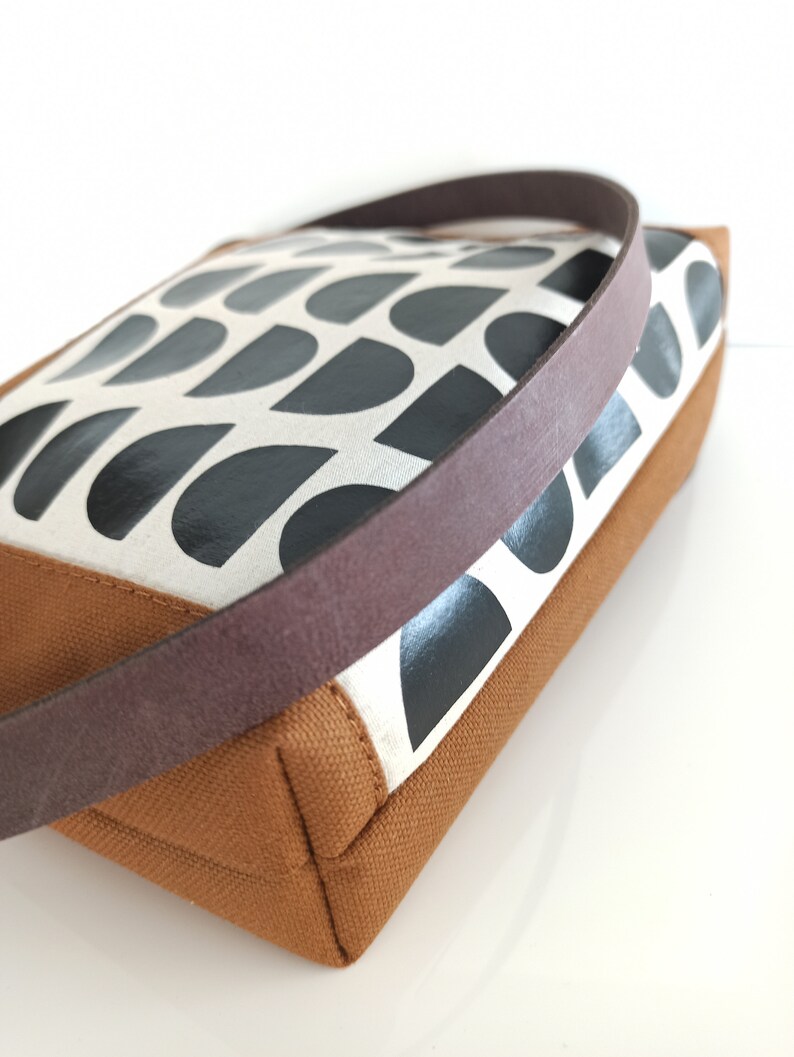May include: A brown canvas tote bag with a black and white geometric pattern. The bag has a brown leather strap.