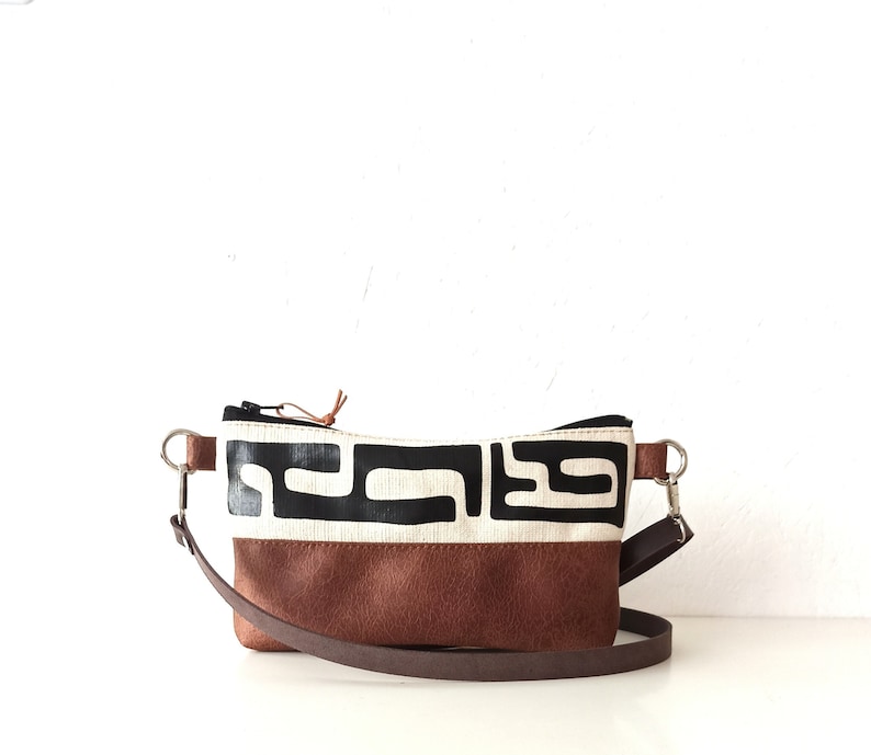 Pode incluir: Uma pochete retangular com base em couro castanho e uma sec&ccedil;&atilde;o superior creme com um padr&atilde;o geom&eacute;trico preto. A bolsa tem uma al&ccedil;a castanha e ferragens prateadas. O puxador do z&iacute;per &eacute; um cord&atilde;o de couro castanho claro.