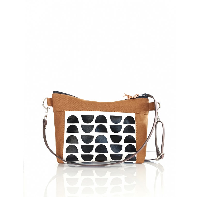May include: A brown canvas crossbody bag with a black and white geometric pattern. The bag has a zipper closure and an adjustable strap.