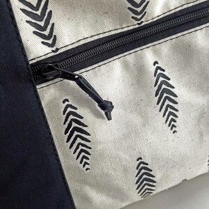 May include: A white canvas zippered pouch with a black zipper and black leaf-shaped patterns. The pouch has a black fabric border.