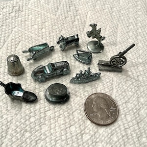 May include: A collection of ten miniature silver-toned metal game pieces including a thimble, wheelbarrow, dog, horse and rider, iron, race car, battleship, cannon, shoe, and top hat, displayed alongside a standard United States quarter coin.
