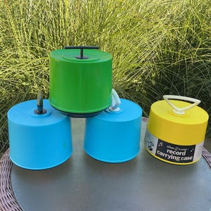 May include: Four round plastic record carrying cases in bright colors: one green with a black handle, two light blue with black and white handles, and one yellow with a white handle. The yellow case features a label reading Disk-Go-Case record carrying case.