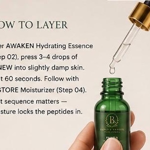 Op de afbeelding: Een groen glazen druppelflesje met een gouden dop en een doorzichtige glazen pipet. De tekst luidt: HOW TO LAYER. After AWAKEN Hydrating Essence (Step 02), press 3-4 drops of RENEW into slightly damp skin. Wait 60 seconds. Follow with RESTORE Moisturizer (Step 04).