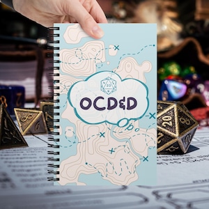 Puede incluir: Un cuaderno de espiral con una cubierta azul claro que presenta un patrón de mapa topográfico beige, rutas de viaje discontinuas y un gráfico central en forma de nube con un icono de dado de veinte caras y el texto "OCD&D".