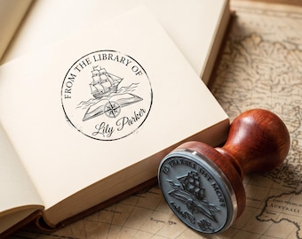 May include: A round rubber stamp with a wooden handle, featuring a design of a sailing ship above an open book with a compass rose. The stamp imprint on the page reads FROM THE LIBRARY OF Lily Parker in black ink.