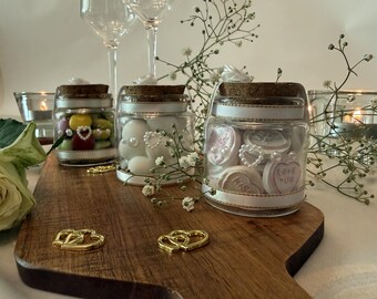 May include: Three small glass jars with cork stoppers, each wrapped in white ribbon and adorned with a small pearl heart charm. The jars are filled with various candies, including heart-shaped sweets with the text LOVE YOU and KISS.