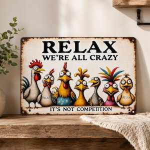 Könnte beinhalten: Ein rechteckiges Metallschild mit abgenutztem Rand zeigt sieben Cartoon-Hühner mit großen Augen. Der Text lautet oben RELAX WE'RE ALL CRAZY und unten IT'S NOT COMPETITION. Zwei der Hühner tragen das Wort RELAX auf ihren Körpern.