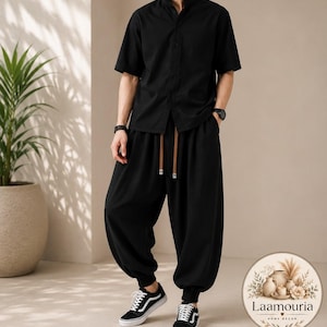 May include: A black short-sleeved shirt with a mandarin collar and a button-down front, paired with black loose-fitting trousers featuring a drawstring waist with brown tips and cuffed ankles, worn with black and white low-top sneakers.