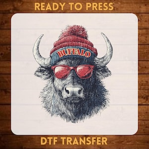 May include: A DTF transfer print featuring a buffalo wearing a red knit beanie with a pom-pom and red sunglasses. The beanie has the word BUFFALO printed in red letters. The text READY TO PRESS and DTF TRANSFER are visible at the top and bottom.