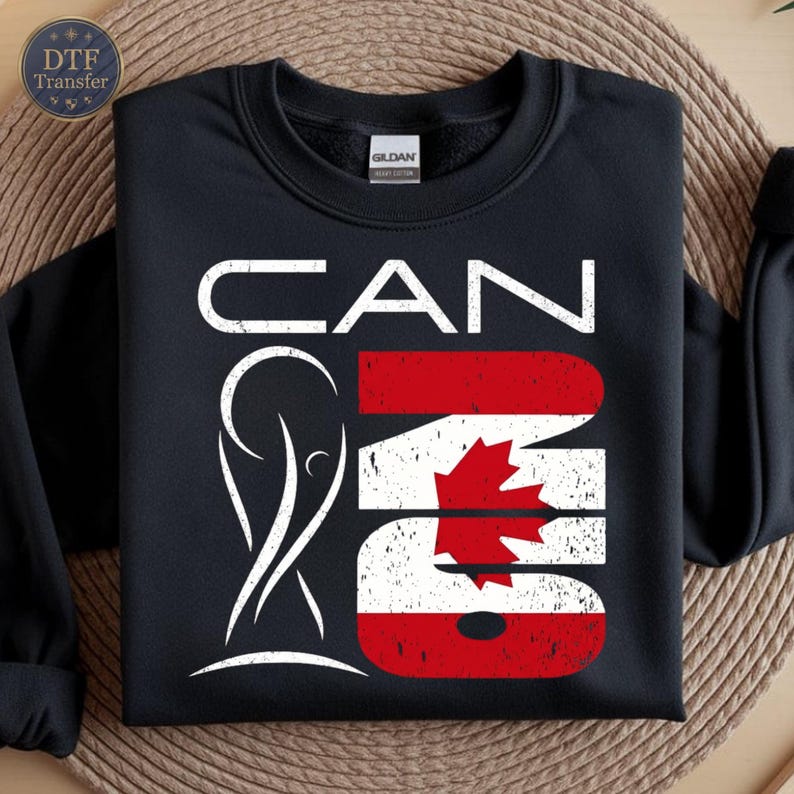 May include: A black crewneck sweatshirt featuring a white graphic with the text CAN and the number 26. The number 26 is filled with the Canadian flag pattern, including a red maple leaf. A white stylized trophy icon is positioned to the left.