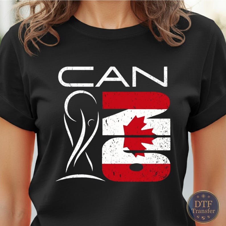 May include: A black short-sleeved t-shirt featuring a white graphic design with the text CAN and the number 26. The number 26 is filled with the red and white Canadian flag pattern, including a maple leaf, and a white trophy silhouette is present.