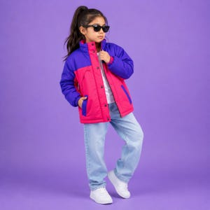 May include: A colour-blocked puffer jacket featuring a vibrant pink torso and deep purple sleeves, paired with light blue denim jeans and white trainers. The jacket includes a front zip closure, snap buttons, and a high collar. Black sunglasses.