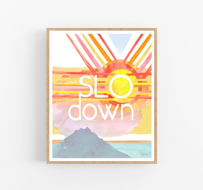 May include: A watercolor painting of a sunset with the words "slow down" in white text. The painting features a yellow sun with red and orange rays, a pink and blue sky, and a blue mountain in the foreground.